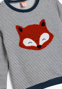 Paskowana szara sweter z teksturowanym wzorem pomarańczowej twarzy lisa. Posiada okrągły dekolt oraz granatowe ściągacze przy rękawach i na dole.