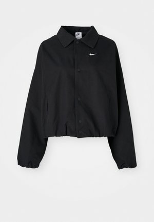 Chaqueta corta negra con cierre de botones en la parte delantera, mangas largas y dobladillo elástico. Cuenta con un pequeño logo blanco de Nike en el pecho.
