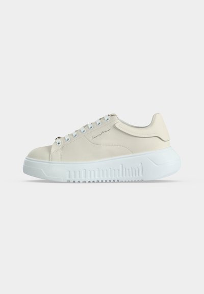 Low-top beige sneaker with white thick sole, lace-up front, and subtle logo script on the side, shown from the outer side.