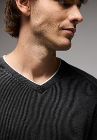 Mörkgrå V-ringad tröja i ribbat stickad tyg med en kontrasterande vit innerribba. Närbild som fokuserar på struktur och design detaljer.
