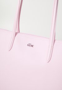 Różowa torba na ramię wykonana z teksturowanego materiału, z dwoma uchwytami i małym haftowanym logo. Gładkie wykończenie z widocznym przeszyciem.