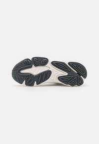 Sneaker sole featuring a black rubber bottom with textured grip patterns and a white midsole. Multi-shaped cutouts enhance flexibility.