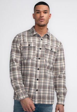 Chemise en flanelle à carreaux marron et crème avec deux poches poitrine et boutons noirs, présentant une coupe décontractée et des manches longues.
