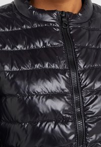 Black padded jacket with a glossy finish, featuring a zip closure and horizontal quilting pattern. Textured fabric adds dimension.