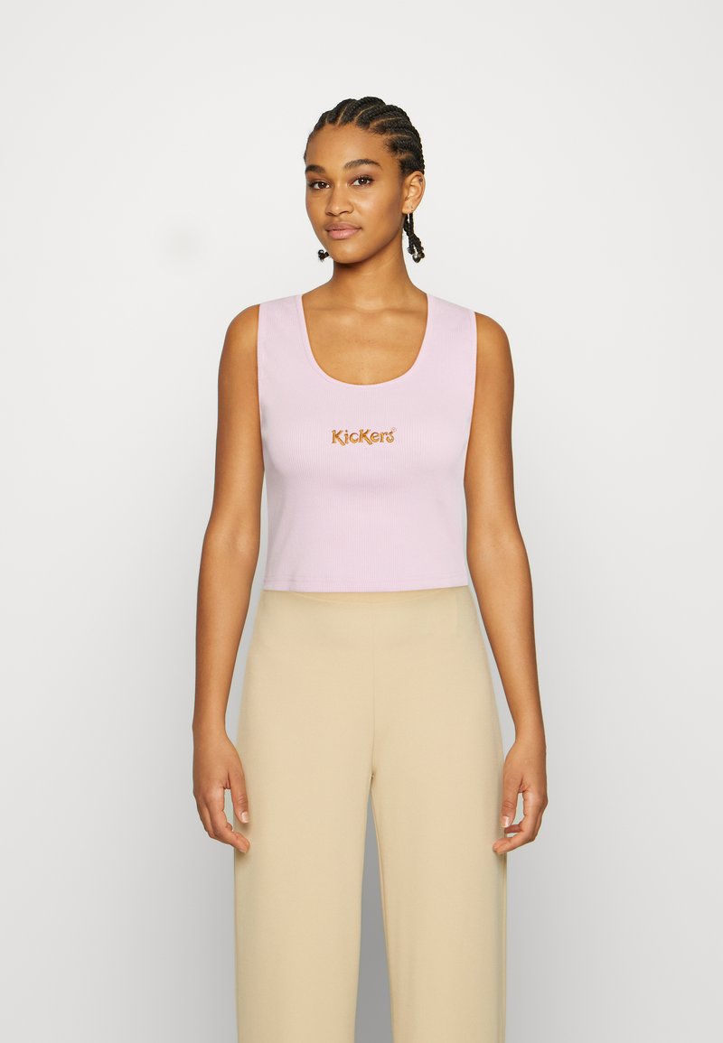 Top cropped rosa com vinco e decote arredondado, apresentando o logo "Kickers" em laranja. Combinado com calças largas beije.