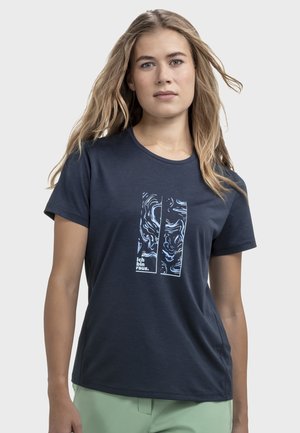 Frau mit langen blonden Haaren, die ein marineblaues T-Shirt mit abstrakten weißen Mustern und dem Text "Ich bin raus." auf der Vorderseite trägt.