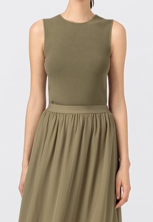 Haut ajusté sans manches vert olive associé à une jupe taille haute, froncée et fluide vert olive sur une personne devant un fond uni.