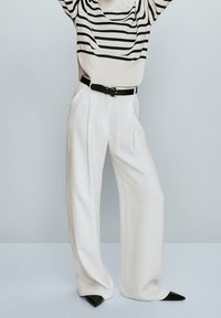 Un pantalon ample blanc associé à un pull surdimensionné à rayures crème et noires. Le pantalon a une coupe ajustée, et le pull présente un col rond.