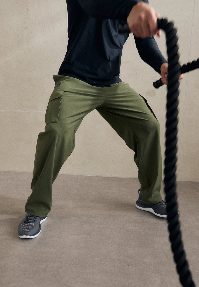 Gröna sportiga cargobyxor gjorda av ett flexibelt material, med sidofickor. I kombination med grå sportskor på en slät yta.