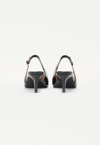 Pantofi cu toc înalt din piele neagră, cu spatele deschis, având o curea subțire și o suprafață texturată, completate de un design elegant al tocului.