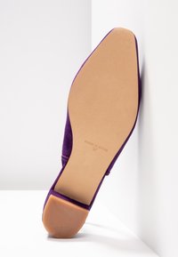 Chaussure plate violette avec semelle beige lisse et petit talon, taille 37, fabriquée en Espagne, positionnée droite contre une surface d'angle blanche.