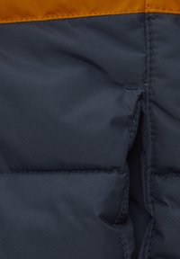 Navyblå puffjacka med en orange övre del, sydda sömmar och en slät, vadderad textur.