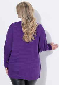 Suéter de punto morado de gran tamaño con textura acanalada, mangas largas y aberturas en los laterales. La parte posterior presenta un ajuste relajado y un dobladillo ligeramente curvado.
