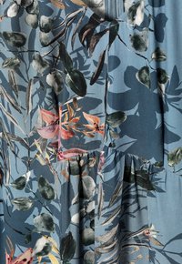 Tissu bleu avec un motif floral comportant des feuilles vertes ainsi que des fleurs roses, orange et jaunes, montrant des plis et des détails de couture.