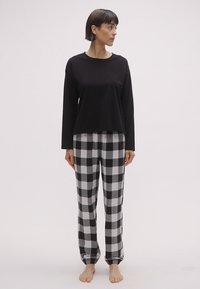 Μαύρο μακρυμάνικο μπλουζάκι συνδυασμένο με γκρι και μαύρο καρό πιτζάμες, με ελαστική μέση και σούρες στους αστραγάλους.