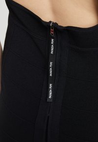 Černé žebrované šaty s viditelným zipem na zadní straně a s branded poutkem. Tkanina má texturovaný vzor pro větší detail.