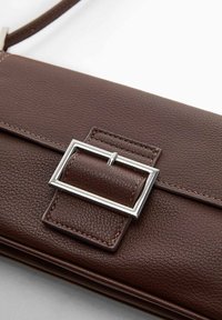 Brązowa skórzana torebka o teksturowanej powierzchni z prostokątnym srebrnym zapięciem na przedniej klapie, pokazana na białym tle.