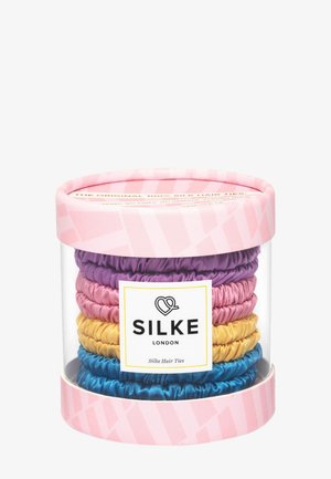 Transparenter zylindrischer Behälter mit pinken Deckeln, der gestapelte Seidenschleifen in Lila, Pink, Gelb und Blau enthält, beschriftet mit "Silke London".