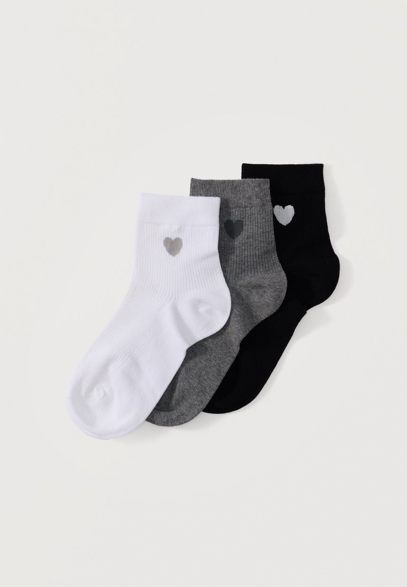 Trois chaussettes chevillées en blanc, gris et noir, chacune avec un petit motif de cœur près de la bordure, posées en chevauchement sur un fond blanc.