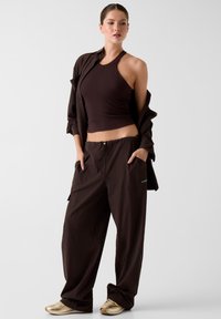 Bruine cropped haltertop met geribbelde textuur, gecombineerd met losse bruine broek met zijzakken en logo. Gestyled met gouden sneakers.