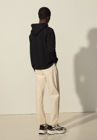 Sudadera negra, pantalones color crema y zapatillas negras con detalles multicolores. Diseño sencillo con un corte relajado y tela texturizada.