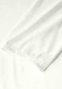 Tissu en coton blanc avec un bord de poignet froncé, présentant une texture lisse et un léger éclat, drapé et doucement froissé.