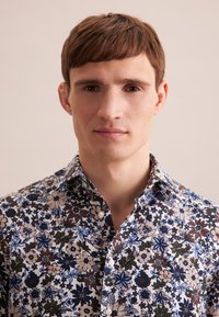 Camicia a fantasia floreale con una combinazione di blu, marrone e verde su uno sfondo chiaro. Button-up con colletto classico e tessuto testurizzato.