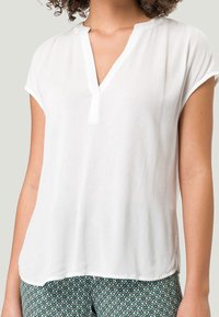 Blusa blanca de manga corta con escote en V, tela texturizada y corte relajado, combinada con pantalones verdes estampados.