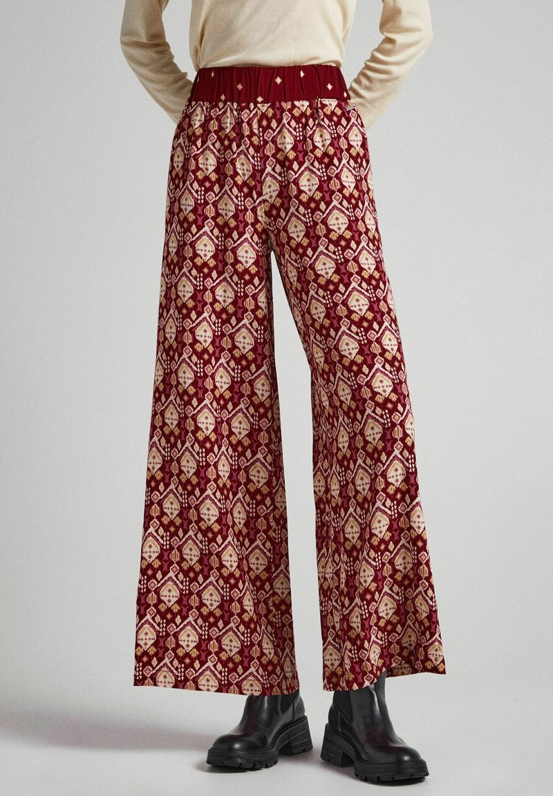 Breda byxor i murrött mönstrat tyg med grädde geometriska former. Elastisk midja, stylat med svarta kraftiga ankelskor.