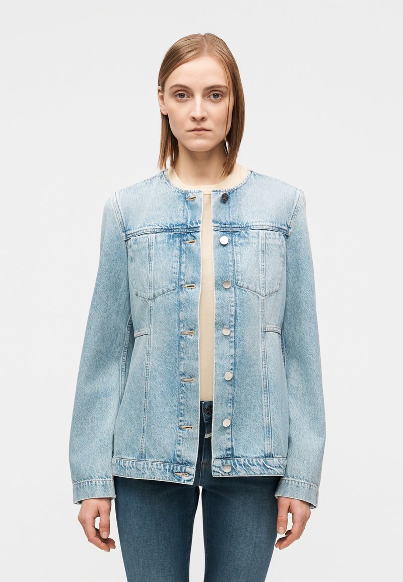 Veste en denim bleu clair avec un col rond, des manches longues, des fermetures à boutons et des poches poitrine. Tissu texturé avec une coupe décontractée.