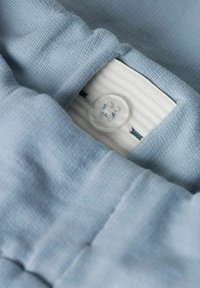 Tessuto azzurro chiaro con una superficie liscia, dotato di una cintura bianca con pieghe e un bottone trasparente al centro.