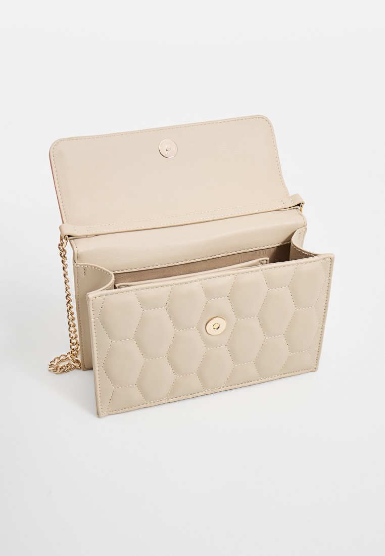 Bolso de imitación de piel acolchado en color beige con un patrón hexagonal, herrajes dorados y una correa de cadena. Cierre de solapa con un detalle de botón a presión.