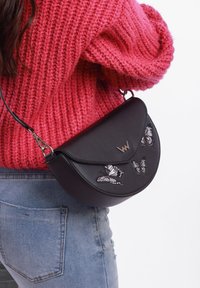 Černá kožená crossbody taška se zaklapávacím víkem, zdobená vyšívanými motivy motýlů a zlatým logem. Ideální na neformální nošení.