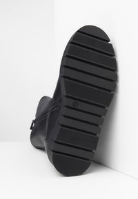 Botte en cuir noir avec une semelle en caoutchouc texturé dotée de rainures pour l'adhérence et un détail de fermeture éclair sur le côté. Taille marquée comme 37.