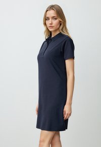Marineblauwe polokleed gemaakt van zachte stof, met een kraag, korte mouwen en een relaxte pasvorm, die tot halverwege de dij komt.