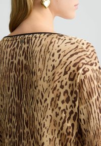 Top beige lavorato a maglia con stampa animale marrone, presenta un bordo nero sullo scollo e un piccolo dettaglio logo metallico sul retro.