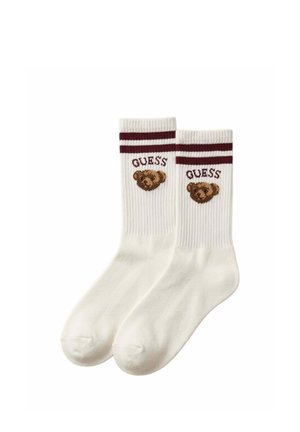 Coppia di calzini bianchi alti con righe marrone scuro in cima, con un volto di orsetto e la parola "GUESS" sopra su ogni calzino.
