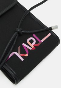 Pochette in tessuto nero con finitura strutturata, caratterizzata da un logo "KARL" multicolore e una chiusura a cordoncino nera con dettagli in metallo argentato.