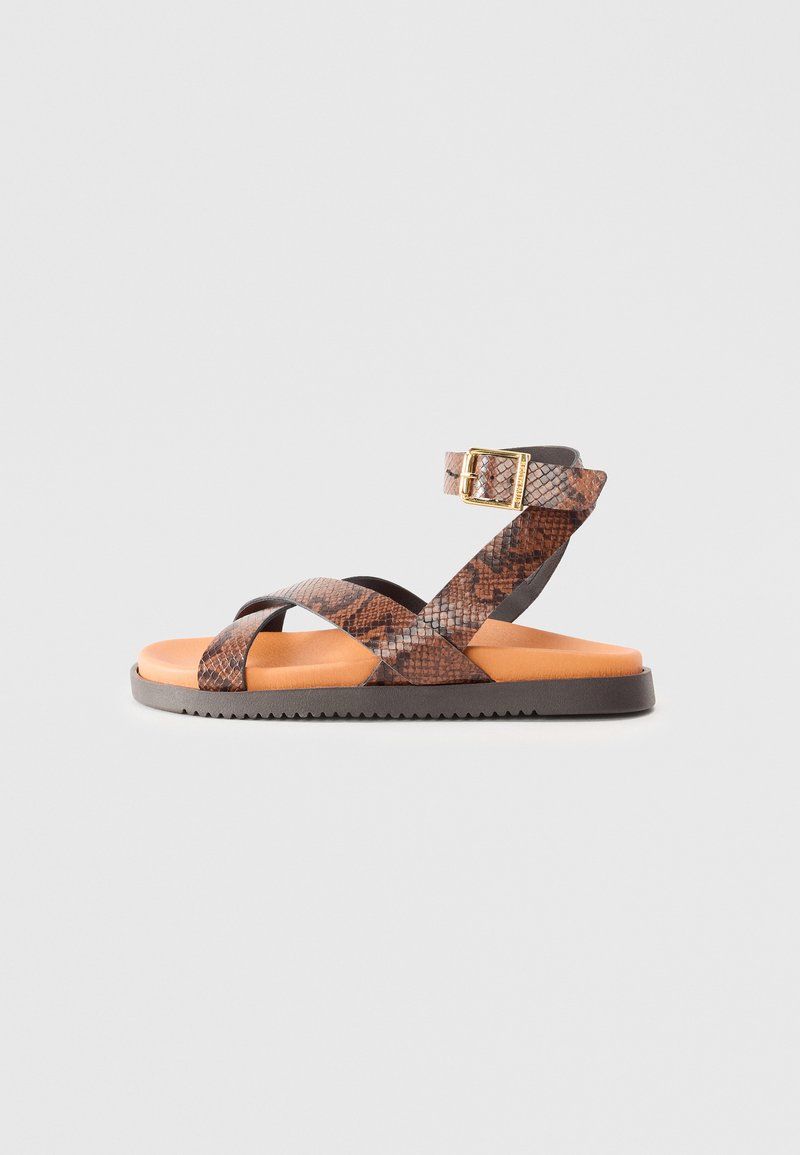 Sandalia de estampado de serpiente marrón y negro con tiras cruzadas, hebilla ajustable y una plantilla acolchada naranja. Suela de goma plana con agarre texturizado.
