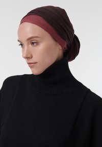 Pañuelo en tonos marrón oscuro y burdeos, hecho de un tejido texturizado, que se lleva con un suéter negro de cuello alto con canalé. Enfoque en la cabeza y los hombros.