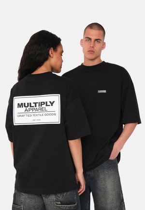 Zwarte oversized t-shirts van katoen. Kenmerken een wit merklong met tekst op de achterkant en een klein label aan de voorkant. Het model poseert rug aan rug.