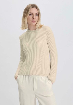 Beige Rippstrickpullover aus weichem Strickmaterial mit Rundhalsausschnitt und langen Ärmeln, kombiniert mit hellen, locker sitzenden Hosen.