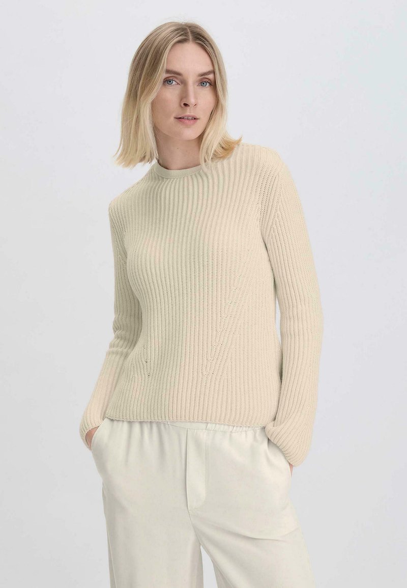 Beige Rippstrickpullover aus weichem Strickmaterial mit Rundhalsausschnitt und langen Ärmeln, kombiniert mit hellen, locker sitzenden Hosen.