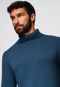 Blauer gerippter Rollkragenpullover mit weicher Textur. Der Kragen ist dick und umgeschlagen und hat eine taillierte Passform, die den Oberkörper betont.