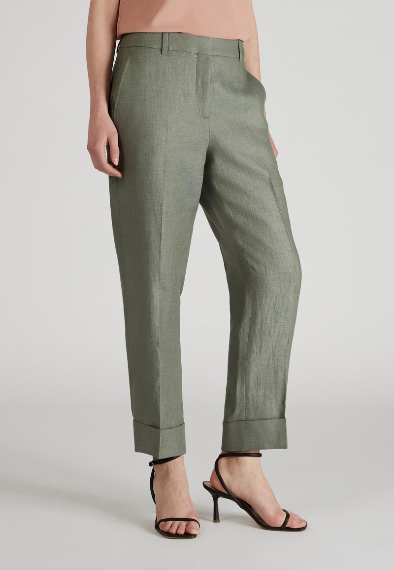 Jasnozielone lniane spodnie o prostym kroju, z przodu fałdy i podwiniętymi mankietami. Połączone z czarnymi sandałami na wysokim obcasie z paskami.