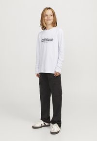 Biały t-shirt z długim rękawem z czarnym logo "Jack & Jones", zestawiony z czarnymi spodniami cargo z bocznymi kieszeniami i gładką teksturą, noszony z trampkami.