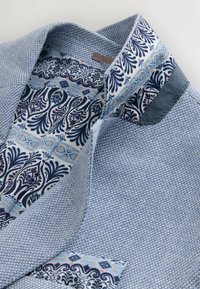 Svetlomodrá košeľa s vnútorným golierom s potlačou v námorníckej modrej, bielej a pastelových farbách; textúrovaná tkanina a kontrastné akcenty goliera.