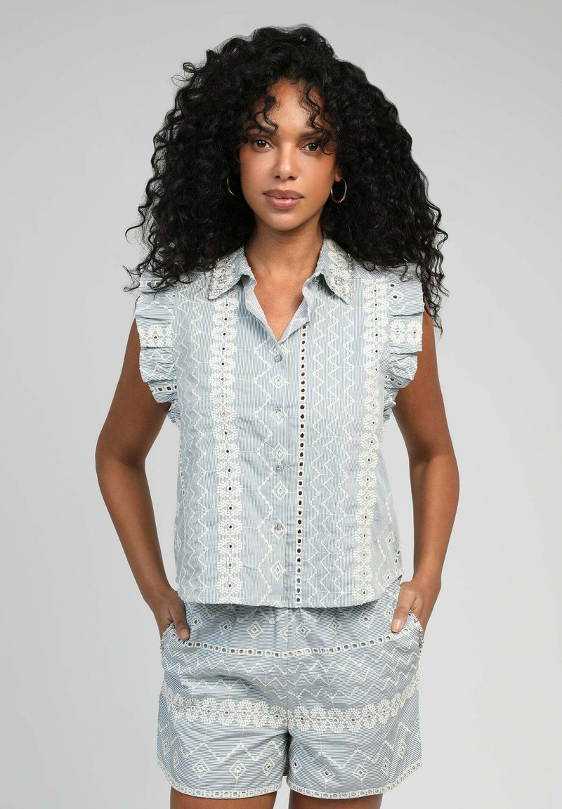 Chemise bleu clair à manches courtes avec des épaules froncées. Présente des broderies blanches, des motifs géométriques, et un short assorti avec des poches.