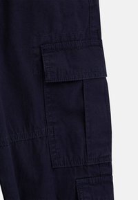 Marine Cargo-Hosen mit mehreren Taschen, sichtbaren Nähten, entspannter Passform und glattem Baumwollmischgewebe. Akzente im flachen Frontdesign.