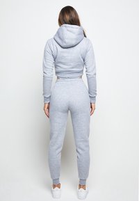 Sudadera gris corta con capucha y mangas largas, combinada con pantalones jogger grises. Textura de tela suave, cinturilla elástica y tobillos ajustados.